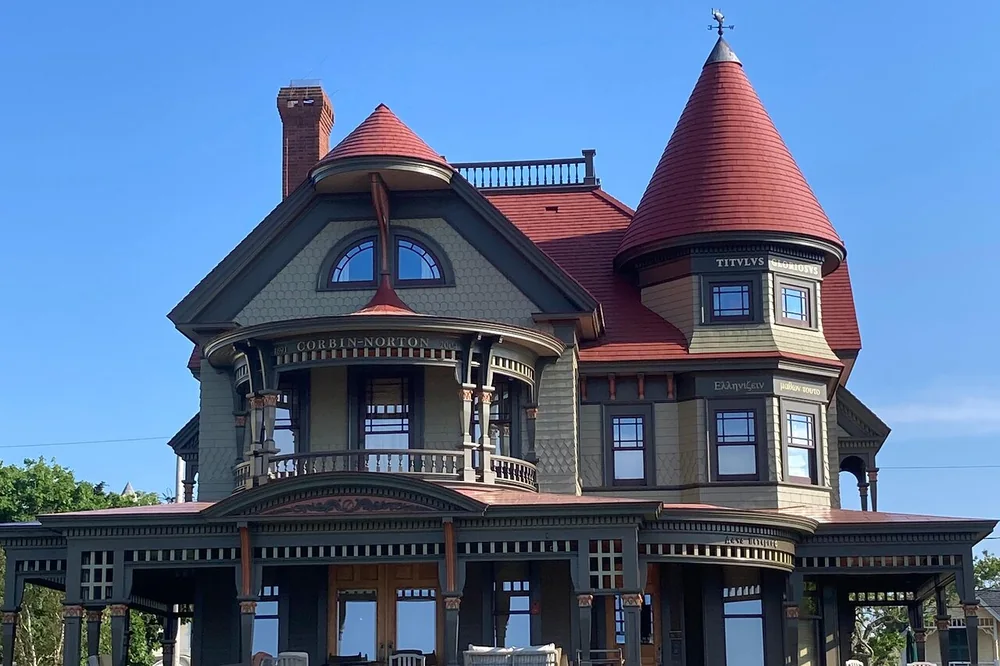 A grand Victorian house with a turret, red roof and wraparound porch